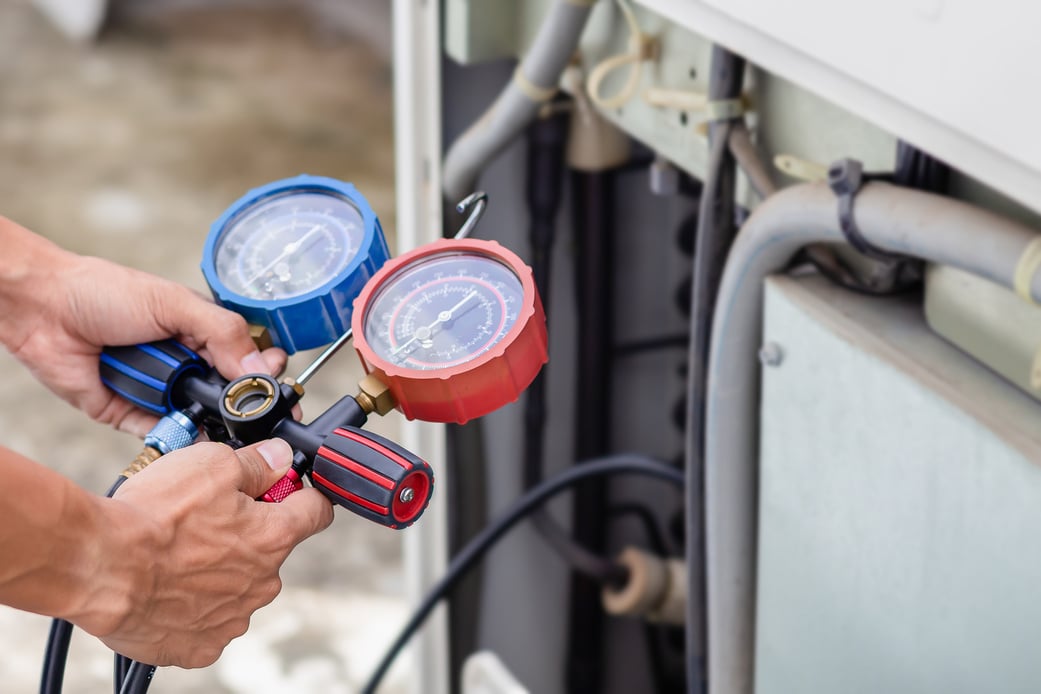 Air conditioning, HVAC service technician using gauges to check refrigerant and add refrigerant.